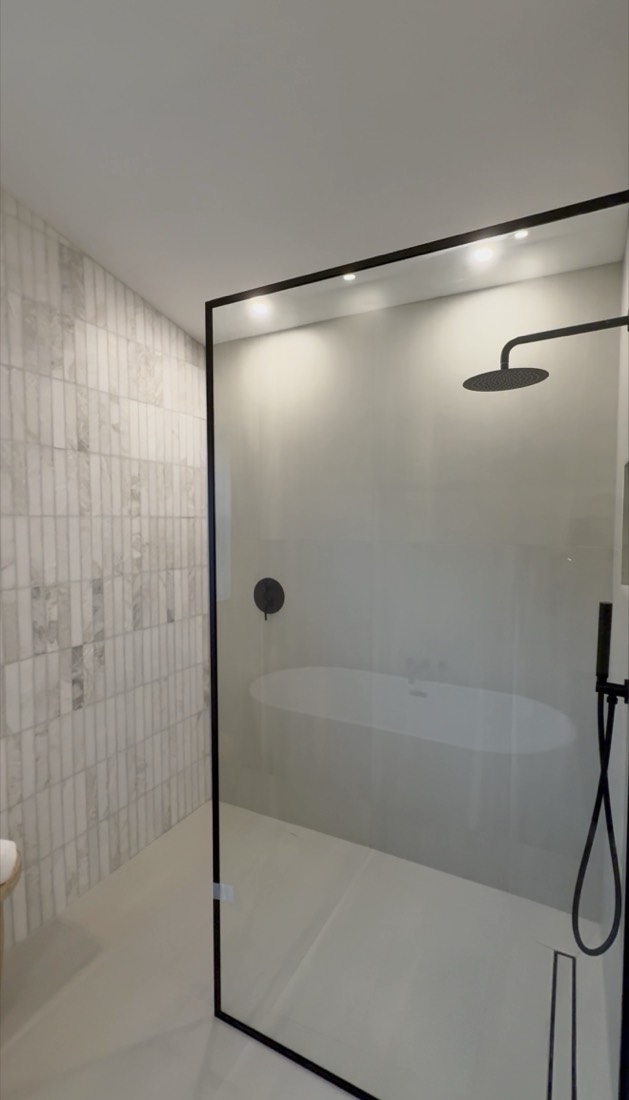 Bathroom remodel in Tampa, FL with a black-framed glass shower enclosure, built-in bench and tiled accent wall