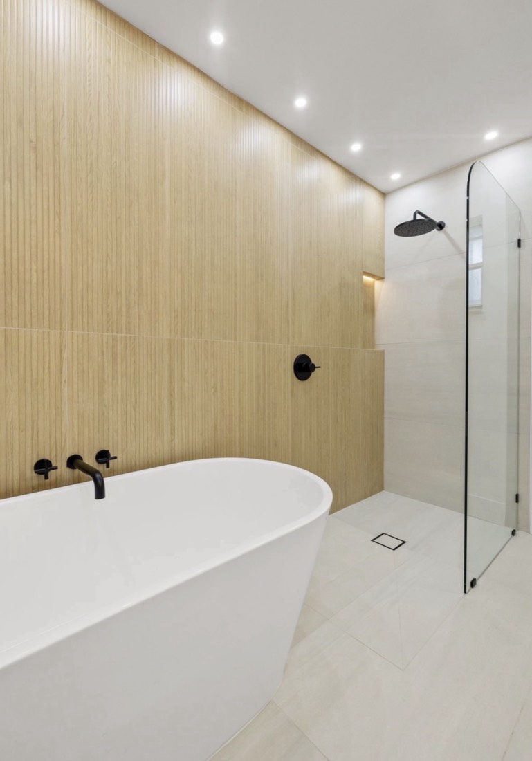 Bathroom remodel in Tampa, FL with a fluted wood-look tile wall, matte black fixtures and a curbless shower