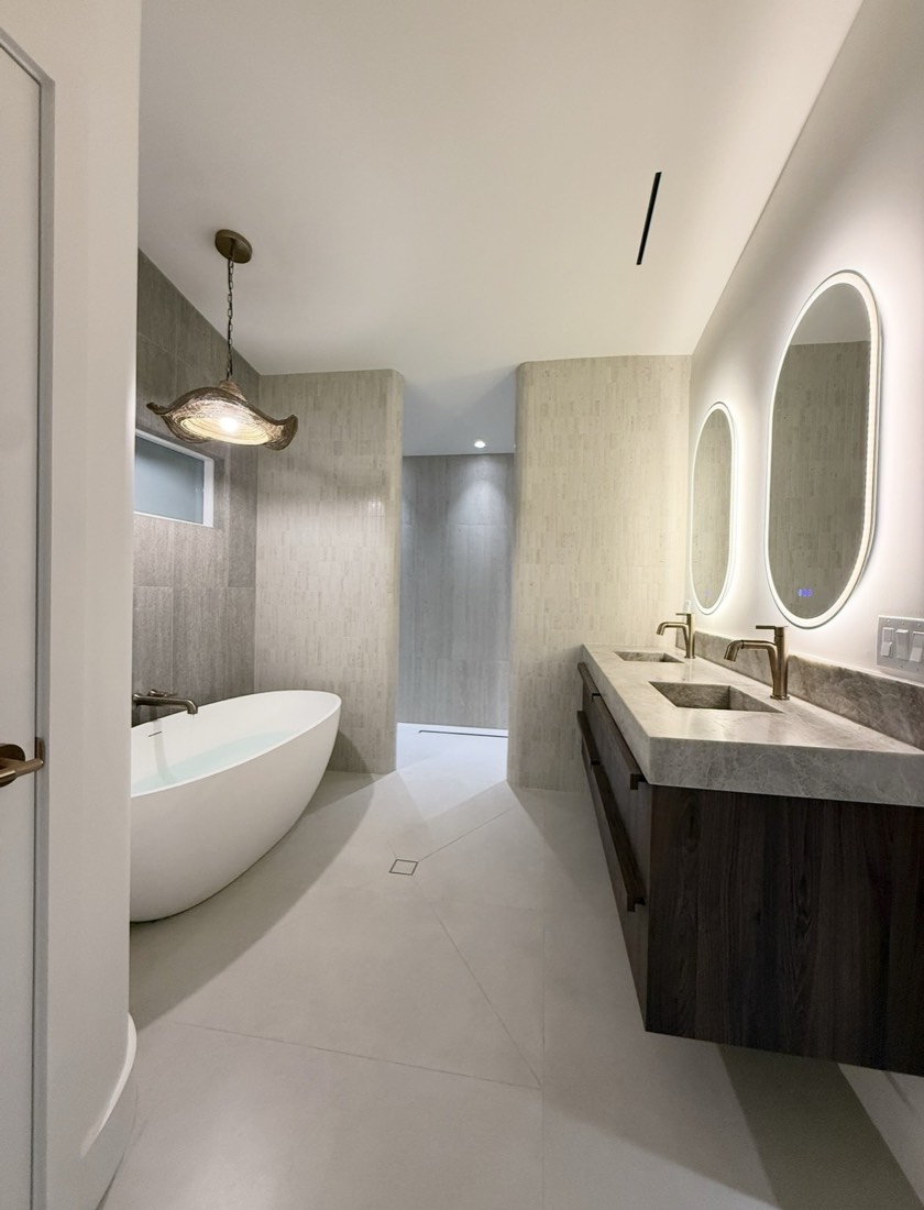 Primary bathroom remodel in Tampa, FL with a floating double vanity, twin backlit mirrors and a freestanding tub